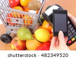 Hand using payment terminal, credit card reader with mobile phone with NFC technology and fresh fruits and vegetables with plastic shopping carts, cashless paying for shopping