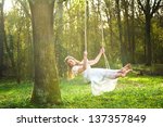 Portrait of a beautiful bride in white wedding dress smiling and swinging in the forest