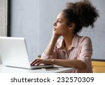 Close up portrait of a young african american woman looking out window when working on laptop