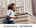 Side portrait of a smiling african american woman walking in the city with cellphone