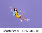 Young beautiful smiling Asian girl floating in mid-air with hand pointing up and down isolated on purple background