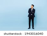 Small photo of Full length portrait of young handsome southeast Asian businessman with arms crossed looking up sideway to copy space on light blue studio background