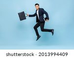 Full length portrait of happy young handsome Asian male office worker running in mid-air holding bag and books in light blue isolated studio background