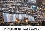 Small photo of Shopping mall exterior with reataurants near fountain in Dubai downtown aerial night timelapse, United Arab Emirates. Illuminated bridge and boats flouting on a water