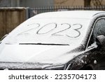 Windscreen wipers and a snow covered car, front view, 2023 inscription. handwritten on snowy window