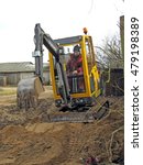 Small photo of NICA, LATVIA - MARCH 21, 2009: Adult man worker is building grovel road in country farm yard with mini excavator.