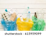 Recycling and ecology. Sorting (segregating) household waste (paper, glass, plastic) into bags captured from above (flat lay). White wooden background with free text (copy) space.
