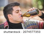 Small photo of Man chug beer from bottle on wooden bench with table in forest park outdoor. Express drinking and fast get drunk lifestyle concept. Real life scene
