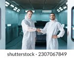 Team of professional automotive painting technician in chemical protecting suit standing in front of the painting chamber together. Car painting and detailing technicians portrait.
