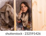Sad young woman in a winter cabin at Christmas staring glumly through a frosted wooden window with a look of loneliness and longing