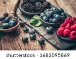 Fresh berries with raspberries, blueberries, blackberries in bowl on a stone stand on wood background.