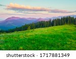 Dawn in the mountains. Wide green meadow in the foreground. Clouds illuminated by the sun. Rich color palette. Summer Carpathians.