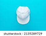 Top view of baseball cap over torquoise blue background. Flat lay top-down composition of white snapback cap. Minimalist flat lay photo of white cap with copy space.