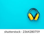 Small photo of Hearing protection industrial earmuffs on turquoise blue background. Top view of yellow protective ear muffs with copy space.
