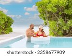 young couple newlyweds spend time together in honeymoon admiring in swimming pool with served floating tray drinks and snacks on tropical island resort in Maldives, breakfast for romantic date, luxury