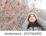Portrait of young beautiful brunette woman in winter clothes walking on nature, girl standing near viburnum bush and looking up