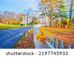 Morning landscape in autumn park. Orange red maple leaves on road. White house on background. Fall season nature scene beauty. Yellow tree alley in city garden Scenery path, sun street. Bunch in fence