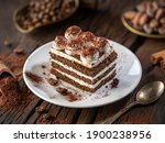 Slice of chocolate cake with tiramisu cream and cocoa powder on wooden table.