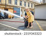 Adorable preschooler girl acting like a fireman holding firehose nozzle and splashing water
