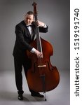 Small photo of Portrait of a man with a double bass on a gray background. Musician with a big double bass.
