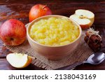 Small photo of homemade apple sauce or apple puree in ceramic bowl over rustic wooden table. top view