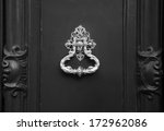 Royal style doorknocker on wooden door. Black and white.