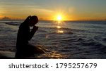 Silhouette of woman kneeling and praying over beautiful sunrise at sea background
