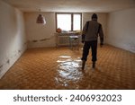 Small photo of Man walks with rubber boots in a flooded tiled basement during flood.