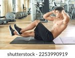 Small photo of Handsome shirtless man doing crunches on exercise mat in gym. Young sporty guy doing crunches with hands on head at gym.