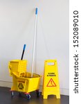Small photo of Mop bucket and wringer with caution sign on black floor in office building