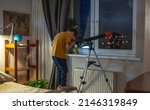 Small photo of Cute boy is looking through a telescope in a room at the night starry sky. Children's passion for space exploration