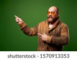 Small photo of Happy male in sweater pointing his hand to empty place against green background