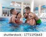 Smiling family of four having fun and relaxing in indoor swimming pool at hotel resort.