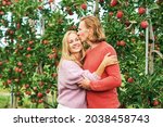 Outdoor portrait of happy young couple posing between fruit trees in apple orchard