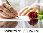 Closeup of the hands of a romantic man writing a love letter to his sweetheart for Valentines Day to be accompanied by a single beautiful fresh red rose