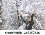 Happy young woman celebrating winter by raising her arms up in the air as she stands outside in beautiful nature in snowy weather.