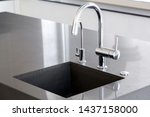 kitchen sink of dark gray stone with chrome faucet in a clean kitchen with a glossy work surface, close up faucet sink.