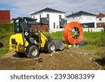 Small photo of Roll of orange fiber optic cable for faster Internet in rural regions. Yellow digger for laying the underground cable in the soil. Barsinghausen, district of Hanover, Germany.