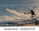 Small photo of silhouette of fisherman pulling his trammel net on the beach shore, during sunset