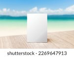 Small photo of Mock up Label the blank menu frame in Bar restaurant. Stand for booklet with white sheet paper acrylic tent card on table wiht blurred beach background can inserting the text or picture.