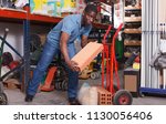Small photo of African-American man putting materials for overhauls on handbarrow in building materials store