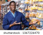 Small photo of Portrait of confident happy seller proffering goods in shop of household materials and tools