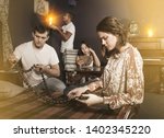 Group of young adults inspecting wooden rosary, trying to find solution of conundrum in escape room with antique furnitures