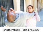 Small photo of Determined young Latina using Krav Maga techniques to protect herself from attacker man on city street. Female self-defense concept..