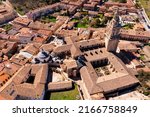 Small photo of Scenic aerial view of medieval Roman Catholic Cathedral of Assumption of El Burgo de Osma with tall gothic bell tower against brownish tiled roofs of residential buildings on sunny spring day, Spain