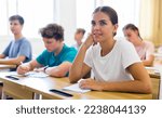 Small photo of Diligent high school student teenage girl studying in college with classmates, making notes of teacher lecture