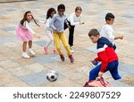 Small photo of Cheerful tween schoolchildren gaily spending time together on warm spring day, playing with ball near school building.