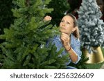 Smiling woman is buying artificial Christmas tree in shop
