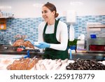 Small photo of Happy female seller in apron standing near counter offering fresh fish flounder