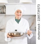Small photo of Confident mature woman in cook outfit showing around hew kitchen